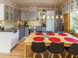 Une cuisine moderne avec des meubles de couleur grise, une table à manger en bois avec des sets de table rouges et un four encastré.