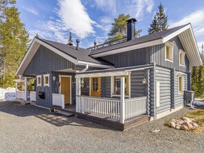 A log cabin with a porch, a chimney, and a view of the surrounding forest. - Rukanlyhty by Interhome (Kuusamo)