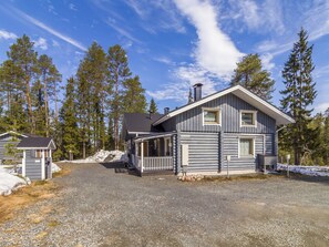 A log cabin with a porch and a small attached structure, surrounded by a gravel driveway and snow patches. - Rukanlyhty by Interhome (Kuusamo)