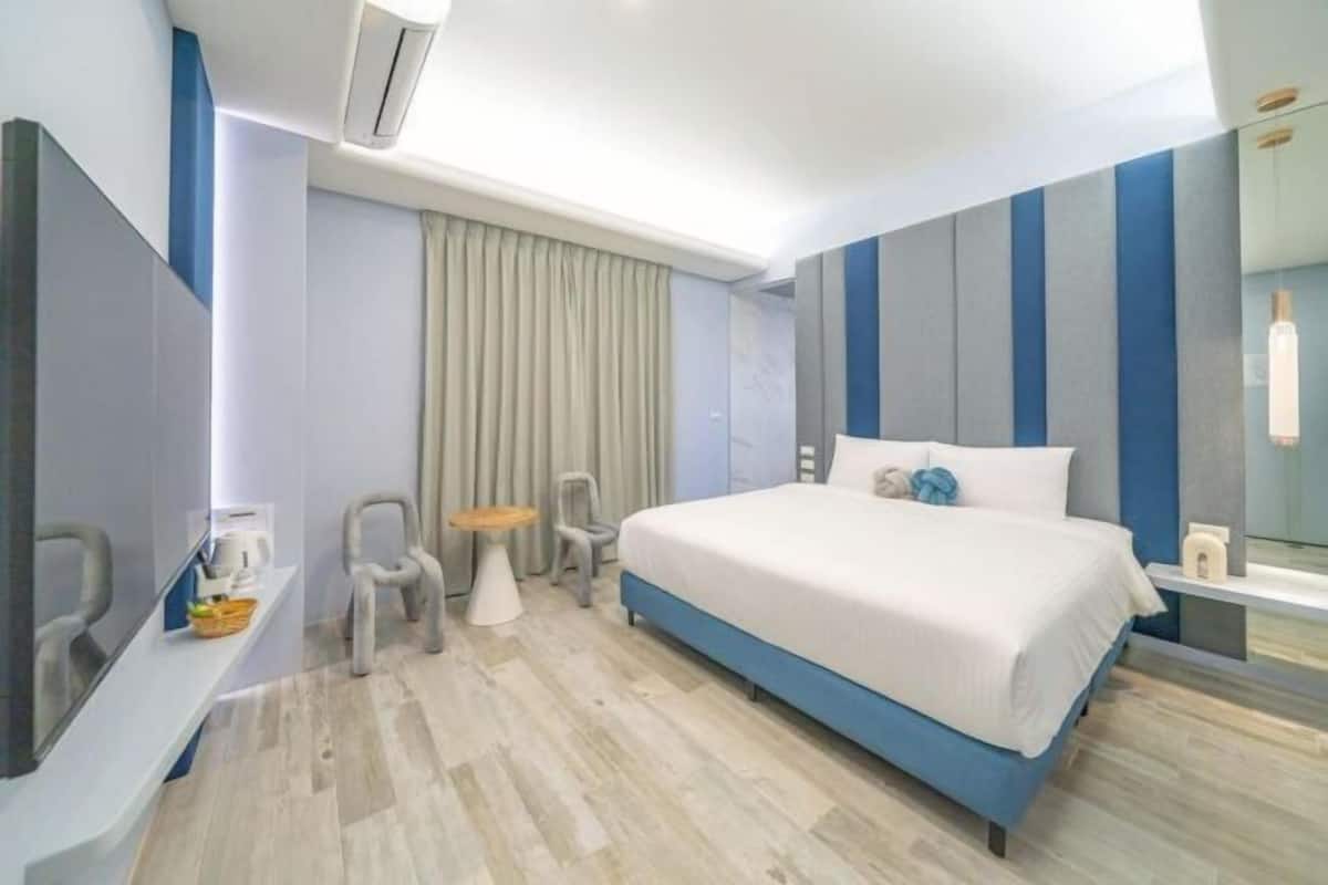 Ein modernes Hotelzimmer mit einem großen Bett, einem Schreibtisch, einem Stuhl, einem kleinen Tisch und einem Spiegel.
