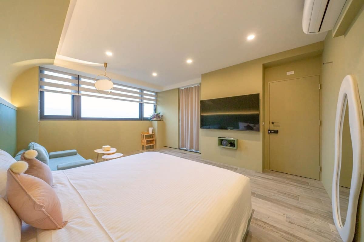 Ein modernes Hotelzimmer mit einem großen Bett, einem kleinen Tisch, einem Sessel, einem Fernseher und einem Kleiderschrank.