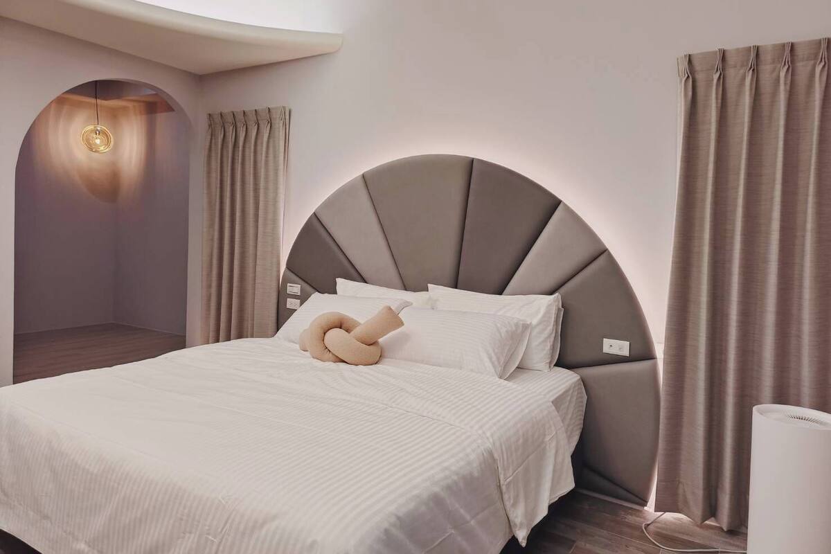 Ein modernes Schlafzimmer mit einem gewölbten Kopfteil, einem Bett mit weißen Bettwäsche und einer Nachttischlampe.