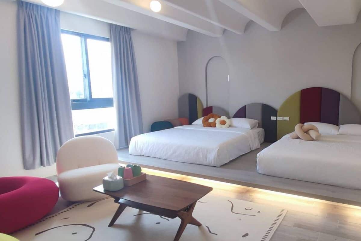 Ein Hotelzimmer mit zwei Betten, einem kleinen Tisch, einem Stuhl und einem Fenster mit Vorhängen.