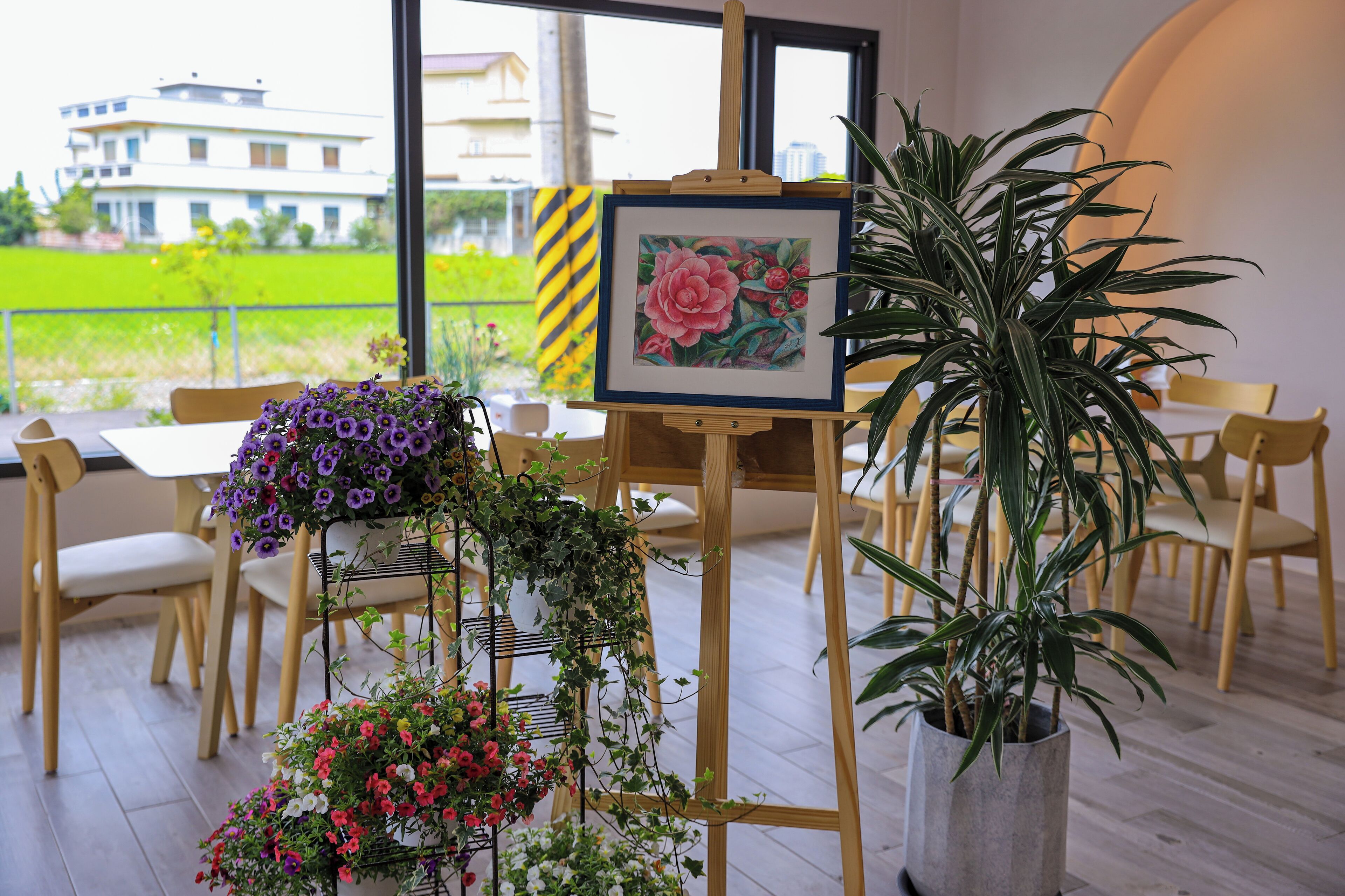 A room with a large window, a painting on an easel, and several potted plants.
