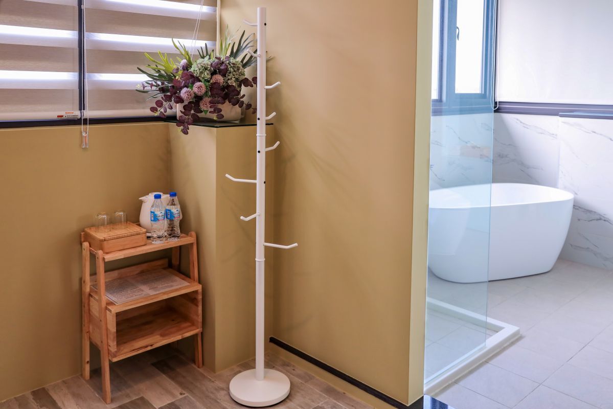 A corner of a room with a wooden shelf, a white coat rack, and a glass shower enclosure.