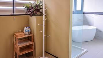 A corner of a room with a wooden shelf, a white coat rack, and a glass shower enclosure.
