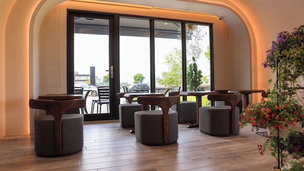 Un intérieur moderne avec un espace salon comprenant des tables rondes et des fauteuils confortables, de grandes fenêtres offrant une vue sur l’extérieur, et une plante en pot agrémentée de fleurs.
