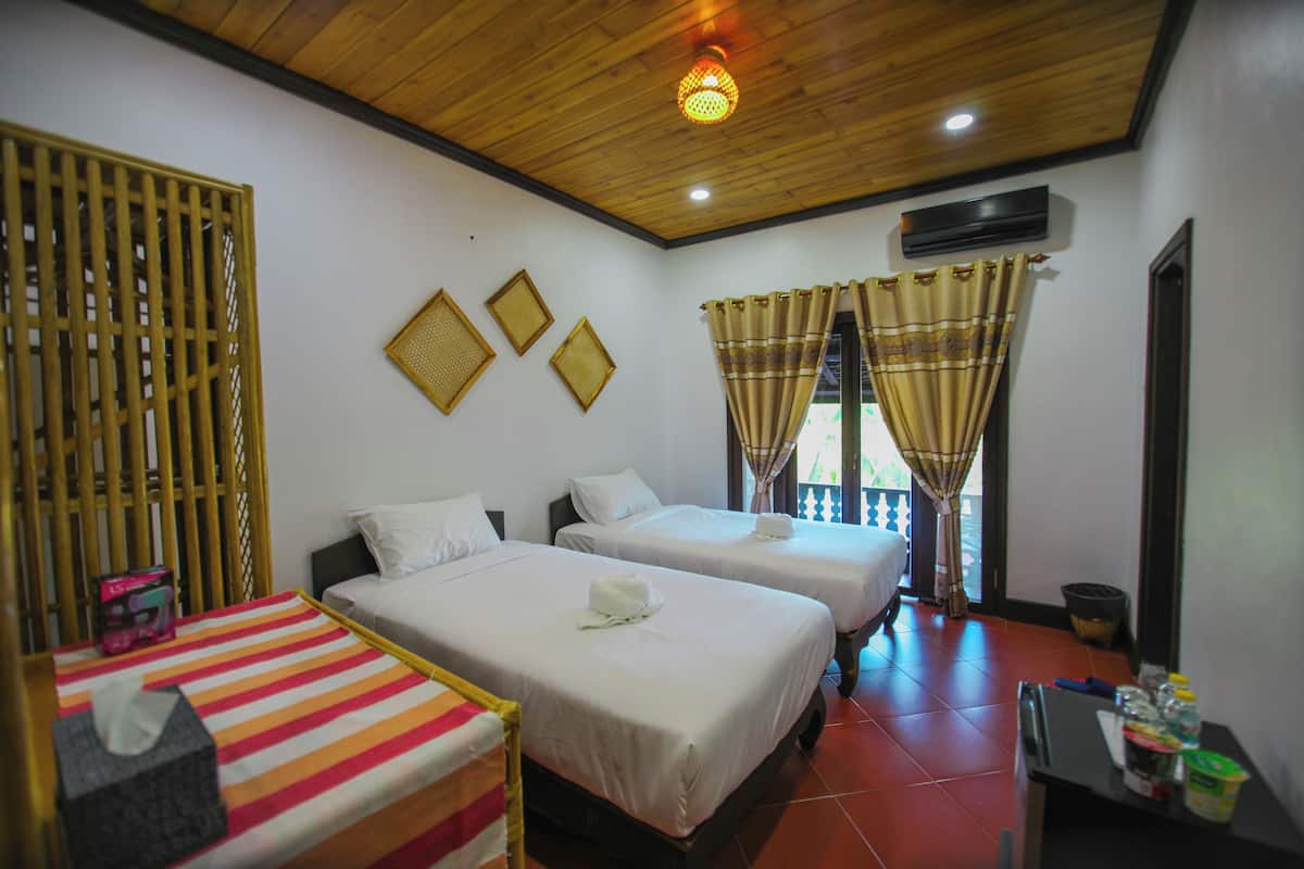 A hotel room with two beds, a wooden ceiling, and a balcony with curtains.