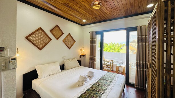 A hotel room with a large bed, wooden ceiling, and a balcony with a view. - Kosy Villa (Luang Prabang)