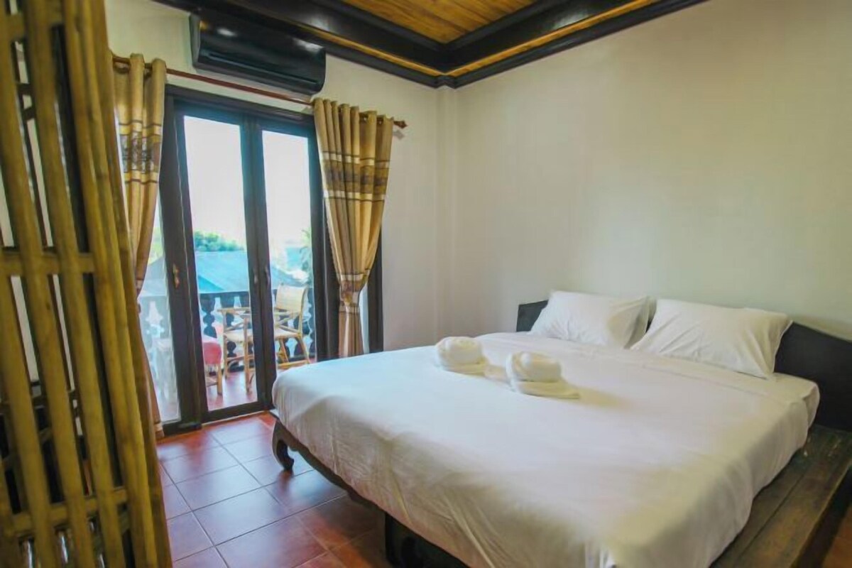 Une chambre d’hôtel avec un lit, du linge de lit blanc et une vue sur l’extérieur, visible à travers une porte vitrée.