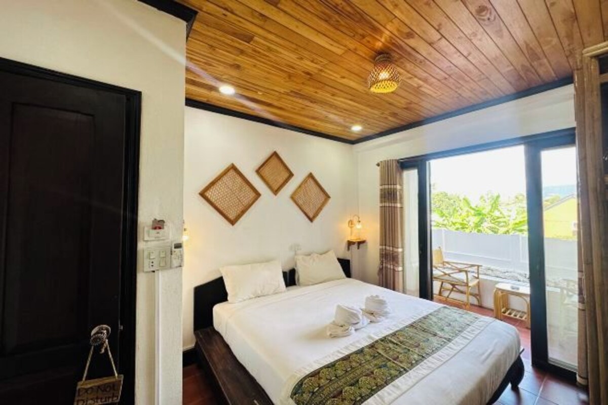 Une chambre d’hôtel avec un plafond en bois, un lit avec du linge de maison blanc, un balcon avec vue et une porte sur laquelle est apposée une pancarte.