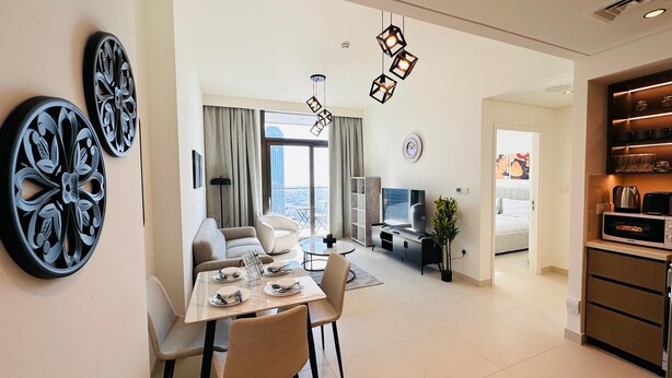 A modern living room with a sofa, dining table, and chairs, a TV, and a kitchen area with a microwave and toaster. - Luxury 1-Bedroom Apartment At Burj Crown. (Dubai)