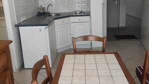 A compact kitchen with white cabinets, a microwave, and a small refrigerator. There is a dining table with chairs in the foreground. - T2 APARTMENT WITH AIR CONDITIONING AND TERRACE + PRIVATE PARKING SPACE (Balaruc-les-Bains)