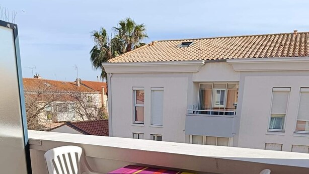 A balcony with a table and two chairs, a tiled floor, and a building with windows in the background. - T2 APARTMENT WITH AIR CONDITIONING AND TERRACE + PRIVATE PARKING SPACE (Balaruc-les-Bains)