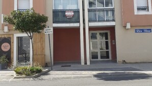 A two-story building with a red and beige facade, a wooden fence, and a sign that reads "ARRET MINUTE". - T2 APARTMENT WITH AIR CONDITIONING AND TERRACE + PRIVATE PARKING SPACE (Balaruc-les-Bains)