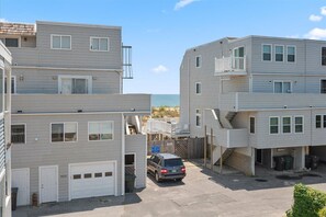 Um edifício residencial de vários andares com garagem, um carro estacionado em frente e vista para a praia.