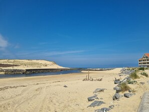 Ein Strand mit sandigem Ufer, einem Felsen und einem Gebäude mit rotem Dach.