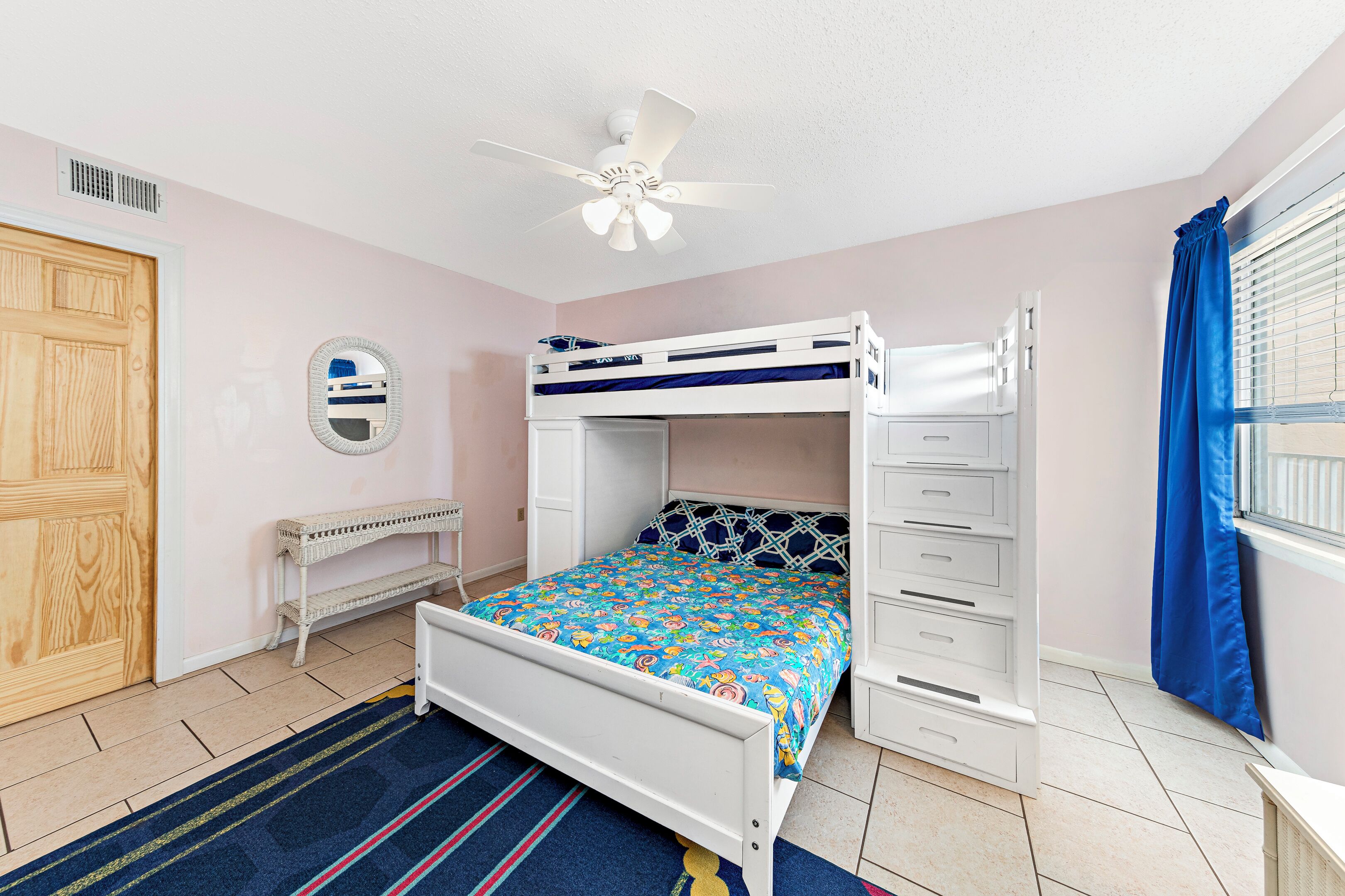 A bedroom with a bunk bed, a ceiling fan, a bedside table, a mirror, and a window with curtains.