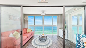 Un salon doté d’une grande fenêtre donnant sur l’océan, d’un canapé rose, d’une table basse ronde et d’une vue imprenable sur la mer.