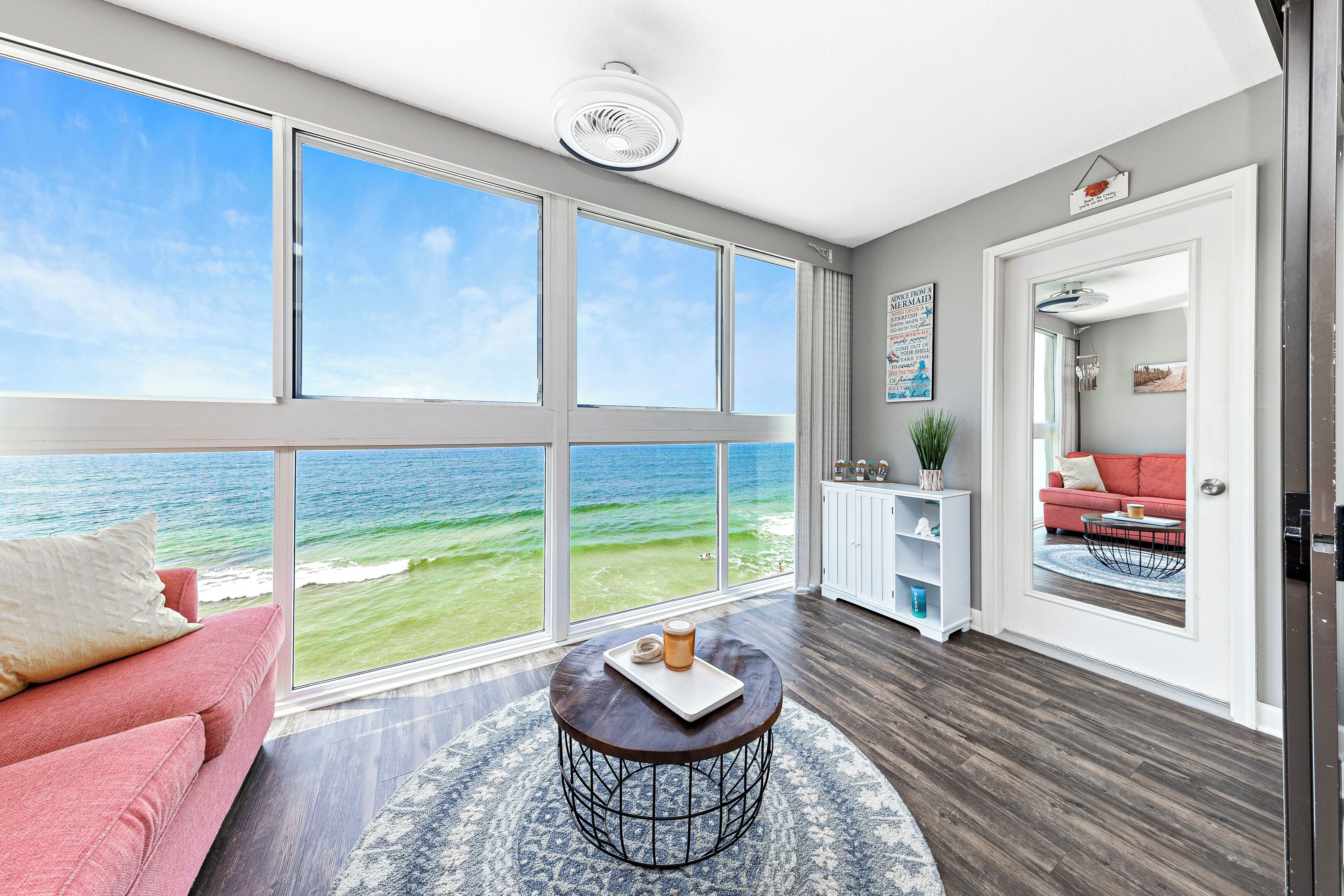A spacious room with a large window overlooking the ocean, a round coffee table, a red sofa, and a white cabinet.