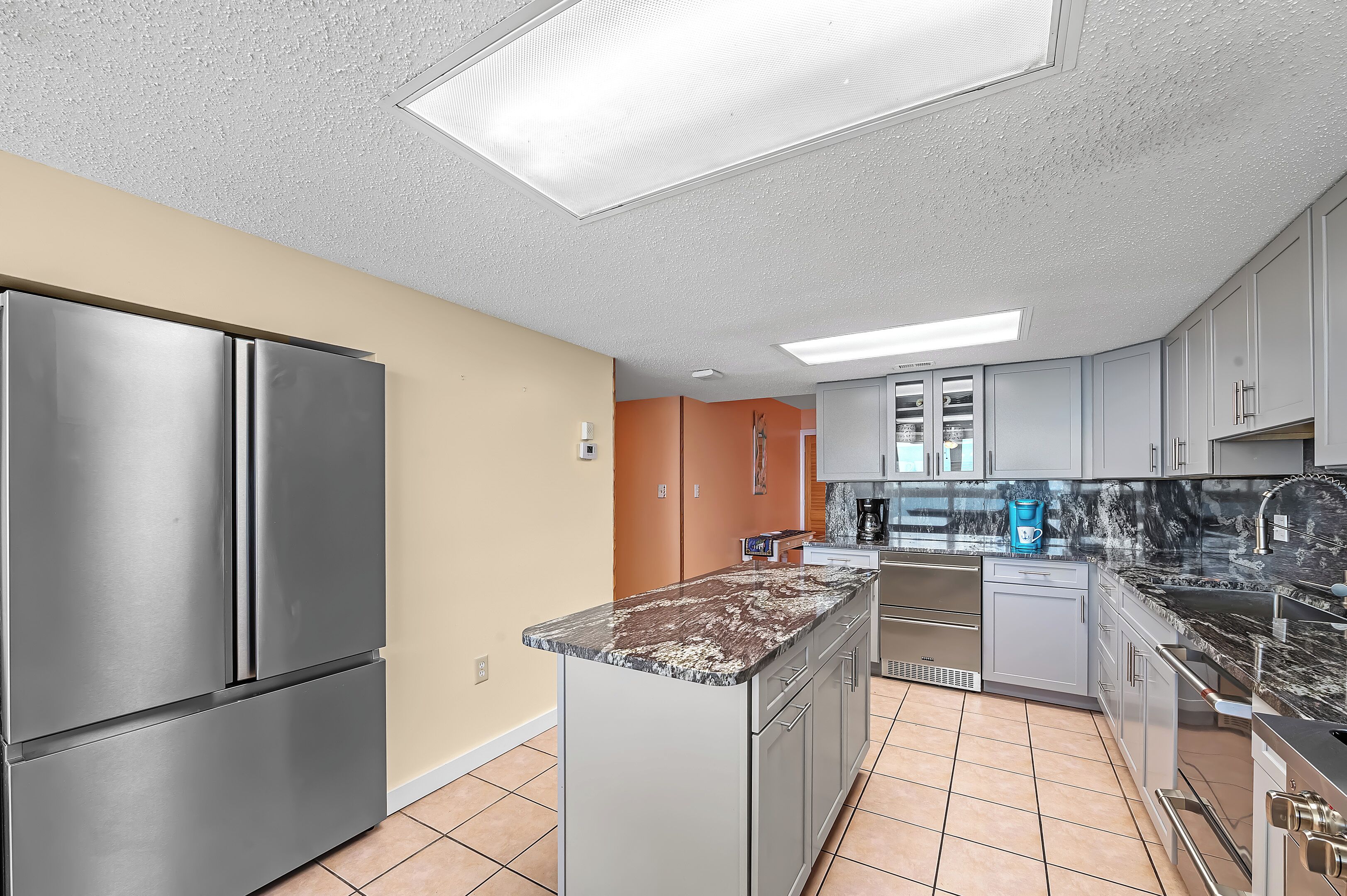 A modern kitchen with stainless steel appliances, a marble island, and light-colored cabinetry.