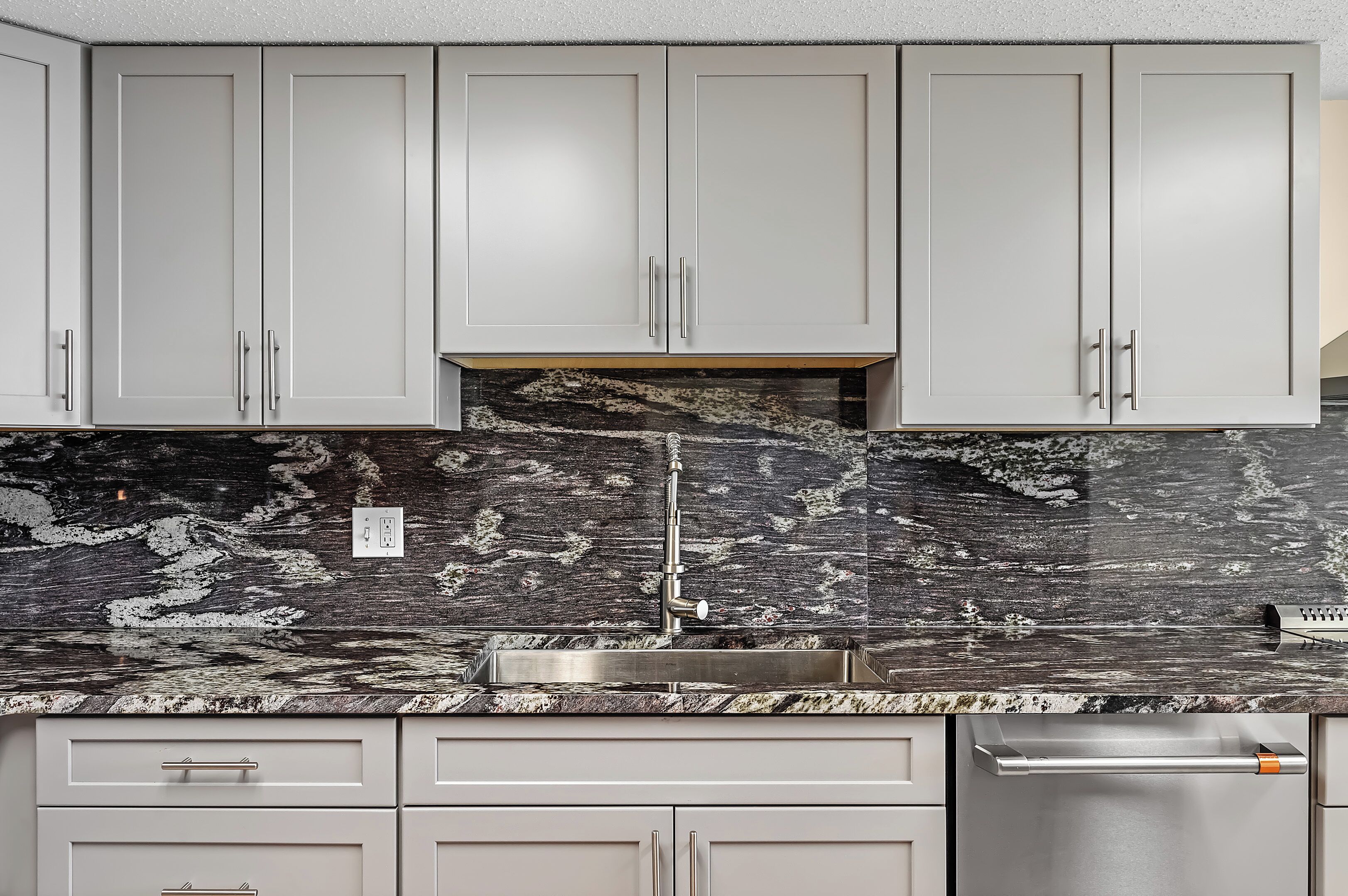 A kitchen with white cabinets, a granite countertop, and a stainless steel sink.