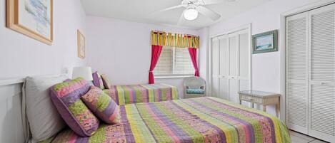 Un dormitorio con dos camas, un ventilador de techo y una ventana con cortinas.