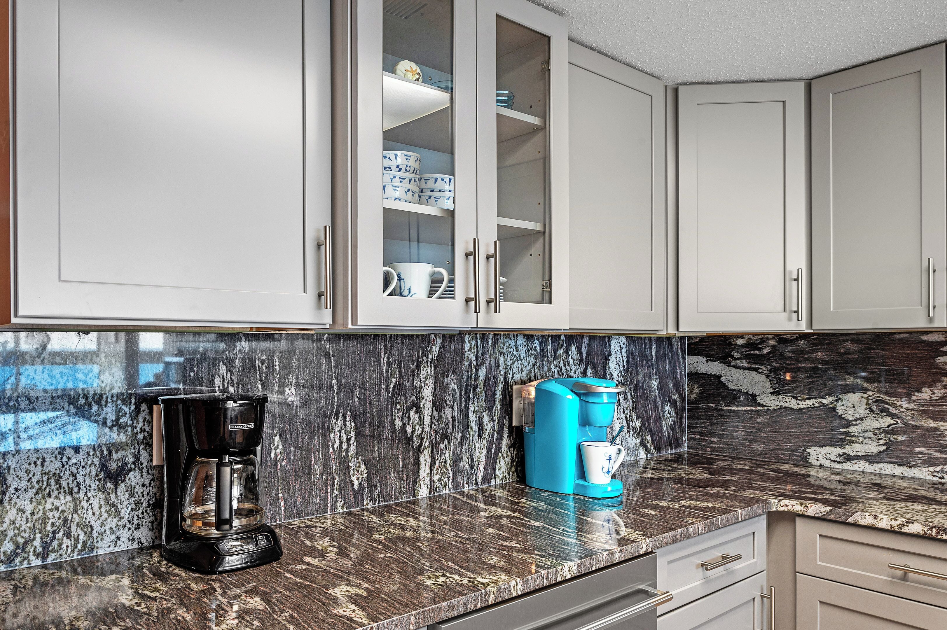 A kitchen with a coffee maker, a blue coffee machine, and a cabinet with dishes.