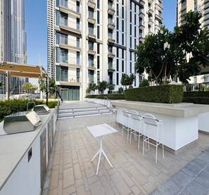 Une terrasse sur le toit avec des espaces de détente en plein air, un coin barbecue et une vue sur les gratte-ciel.