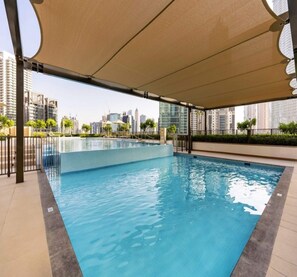 Une piscine offrant une vue sur les gratte-ciel de la ville, entourée d’une zone abritée dotée d’un auvent.