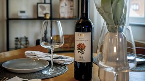 Une table à manger avec une bouteille de vin, un vase de fleurs et des assiettes vides.