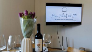 Une table à manger avec une bouteille de vin, des verres et un vase de fleurs. L’écran de télévision affiche l’émission « Prime Retreats UK 110 », accompagnée d’un message sur les réussites dans le domaine immobilier.