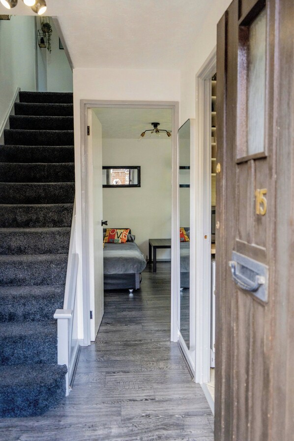 Un pasillo que conduce a un dormitorio con una cama, una escalera y una puerta de madera.