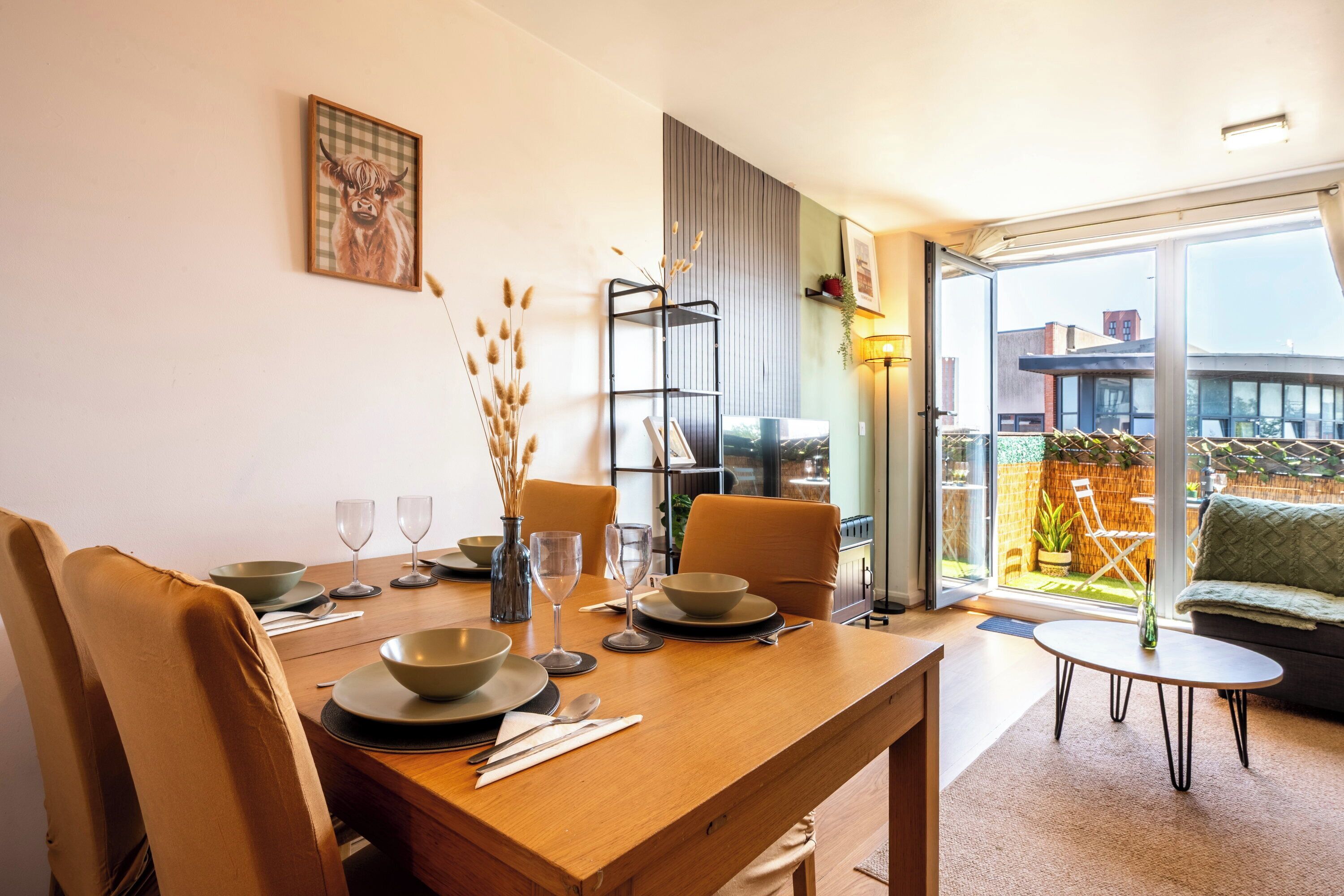 Un comedor con mesa de madera para dos, sofá y vistas al exterior.