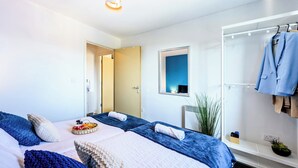 Habitación de hotel moderna con dos camas, un espejo, perchero y una pequeña planta.