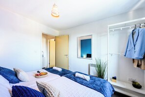 A modern hotel room with two beds, a mirror, a coat rack, and a small plant.