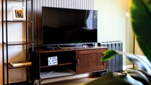 Una sala de estar moderna con un televisor de pantalla plana sobre un mueble de madera, una estantería y una pequeña planta.