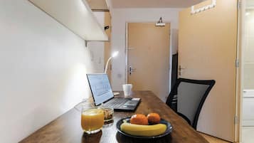 A wooden table with a laptop, a glass of orange juice, a plate with a banana and two oranges, and a black mesh chair.