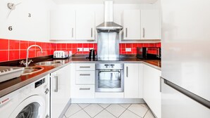 Una cocina moderna con armarios blancos, una campana extractora de acero inoxidable, un horno integrado y una lavadora.
