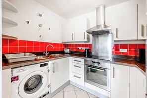 Ett modernt kök med en tvättmaskin från Bosch, vitvaror i rostfritt stål och ett rött kakel som stänkskydd.