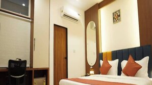 A hotel room with a large bed, a desk with a chair, an air conditioning unit, and a mirror on the wall. - Hotel Rudravue (Indore)