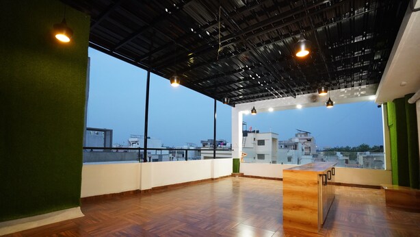 A spacious room with a wooden floor, a green accent wall, and a view of the cityscape through large windows. - Hotel Rudravue (Indore)