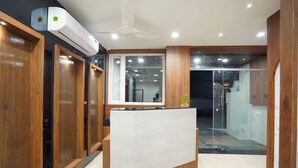 A reception area with a wooden reception desk, glass doors, and an air conditioning unit. - Hotel Rudravue (Indore)