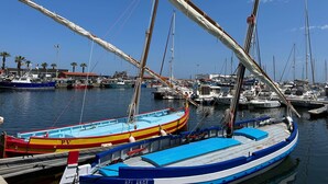 A marina with multiple boats docked, including a red and yellow boat labeled "PV" and a blue boat labeled "BEL ANGE".