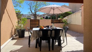 An outdoor patio with a table and chairs, a large umbrella, and potted plants.