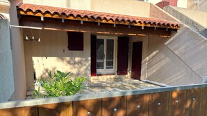 A covered patio area with a wooden fence, a small garden, and a door leading to a building with a tiled roof.