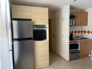 Uma cozinha compacta com geladeira embutida, micro-ondas, forno e uma televisão pequena.