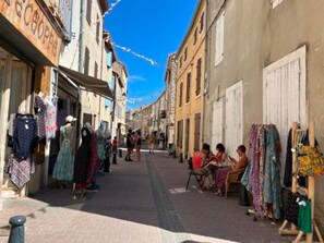A narrow street with shops on both sides, some with clothing displays.