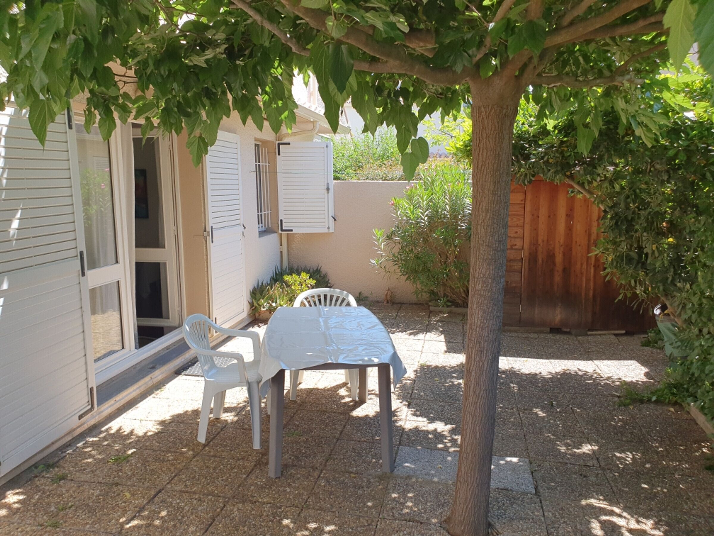 A patio with a table and chairs, a tree, and a building with shutters.