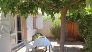 A patio with a table and chairs, a tree, and a building with shutters. - Saint-Cyprien: Ground Floor T3, Terrace, Parking, 600m from Beach (Saint-Cyprien)